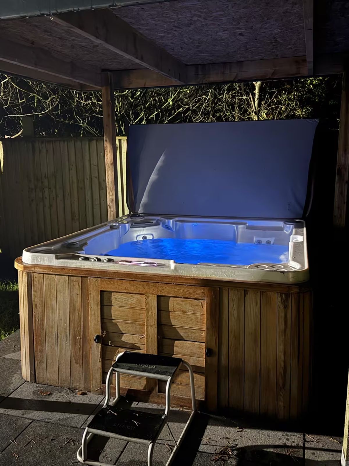 The covered hot tub, lit blue, with steps up